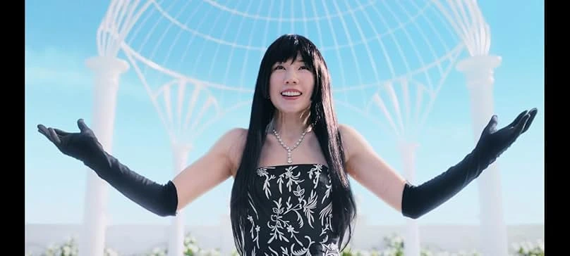 Mira Kano from Alice in Borderland smiles with arms spread wide, wearing a black and white dress, black opera gloves, and a diamond pendant, set against a background of soft blue skies and white architectural domes.