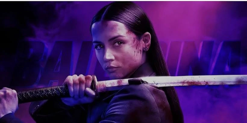 Close-up portrait of Ana de Armas as the character Ballerina from the movie of the same name, holding a katana, and staring forward with a serious expression. Abrasions are visible on her face. The title "BALLERINA" is in large, bold, stylized letters in the background.