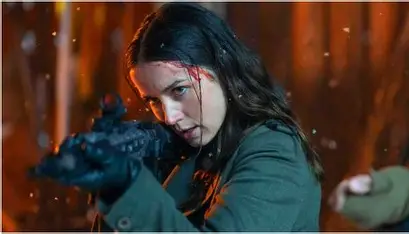 Ana de Armas as a determined Ballerina movie review character, aiming a rifle with focused intensity, slight blood evident near her hairline, set against a blurred background of orange and white hues possibly indicating fire or chaos.