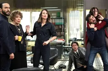Scene from a hidden Netflix shows in 2025; group of seven people inside an office with concerned expressions. On the left, a man with a beard appears worried, next to an older woman who raises her hand as if to scold; a woman in a jumpsuit looks ahead seriously in the center; on the right side, a man carries a woman on his back, both with fearful expressions, and a man lies on the floor with a concerned expression.