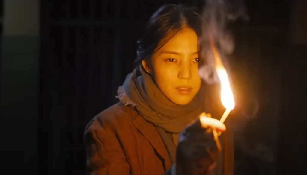 A young woman in a period brown jacket and scarf holds a lit match, casting an orange glow on her face, her expression concerned; featured in a list of the Top 5 Korean Dramas available on Netflix in 2025.