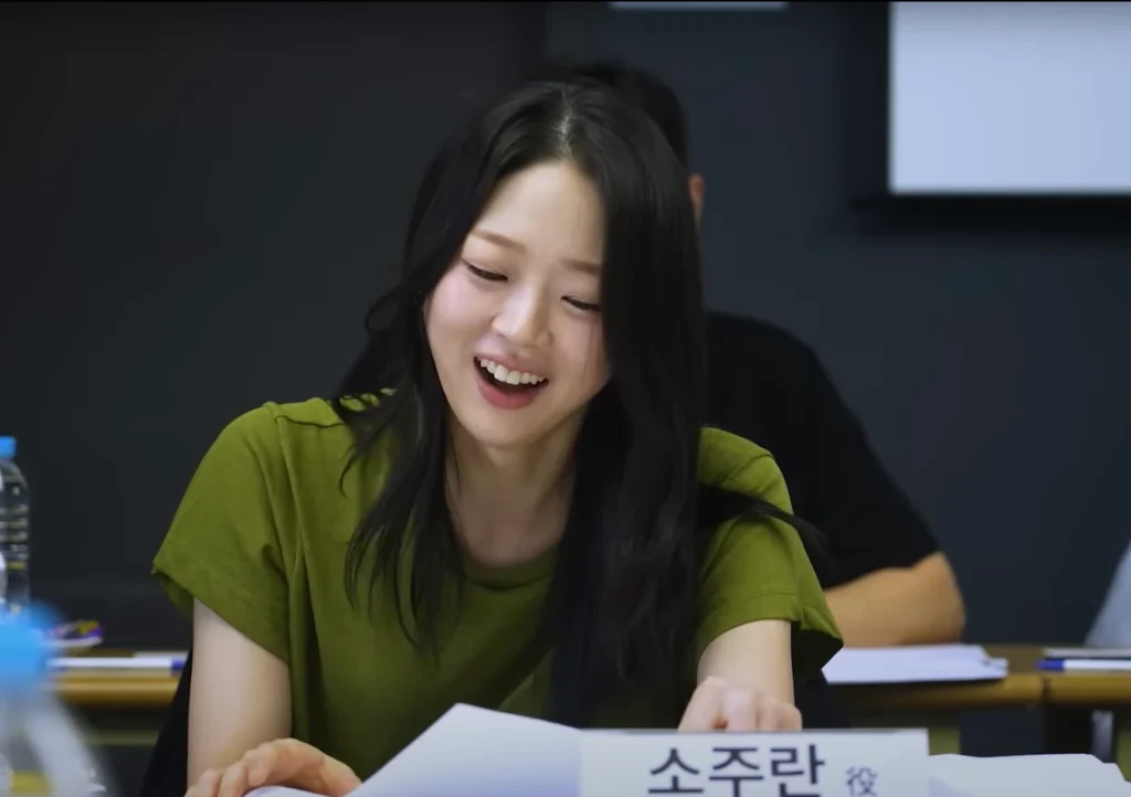 Actress smiling during "All of Us Are Dead Season 2" table read, wearing green shirt, with black hair, reading script.