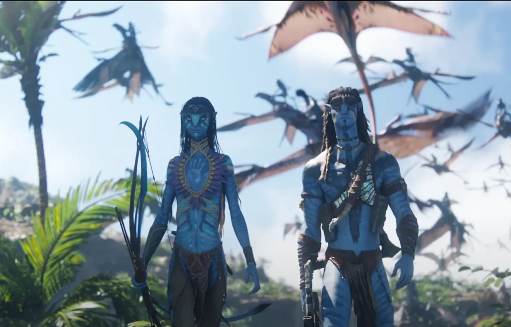 Two Na'vi characters from the Avatar 3 trailer stand outdoors with neutral expressions; the character to the left holds a bow and arrow, and winged creatures fly in the background sky.
