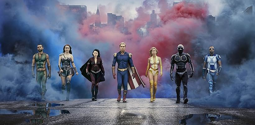 Promotional image for *The Boys* presents seven superheroes, The Seven, walking toward the viewer, against a backdrop of a grimy, urban scene obscured by swirling blue and red smoke. From left to right: A-Train, a muscular dark-skinned man with a trimmed beard; Starlight, a light-skinned woman with long blonde hair; Queen Maeve, a fair-skinned woman with dark hair; Homelander, a fair-skinned man with blonde hair and a cape; Stormfront, a fair-skinned woman with blonde hair; Black Noir, obscured by a full-body black suit; and The Deep, a muscular dark-skinned man with sunglasses. Each character is depicted with a serious expression.