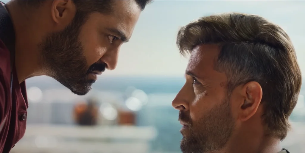 Close-up still from the War 2 trailer featuring Jr. NTR and Hrithik Roshan facing each other with serious expressions.
