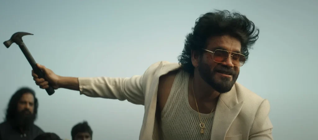 Nagarjuna, appearing in the "Coolie Trailer Rajnikanth", smiles and holds a hammer menacingly, wearing sunglasses, a white suit jacket, and a tank top, with a gold necklace visible. Other people stand blurred behind him.