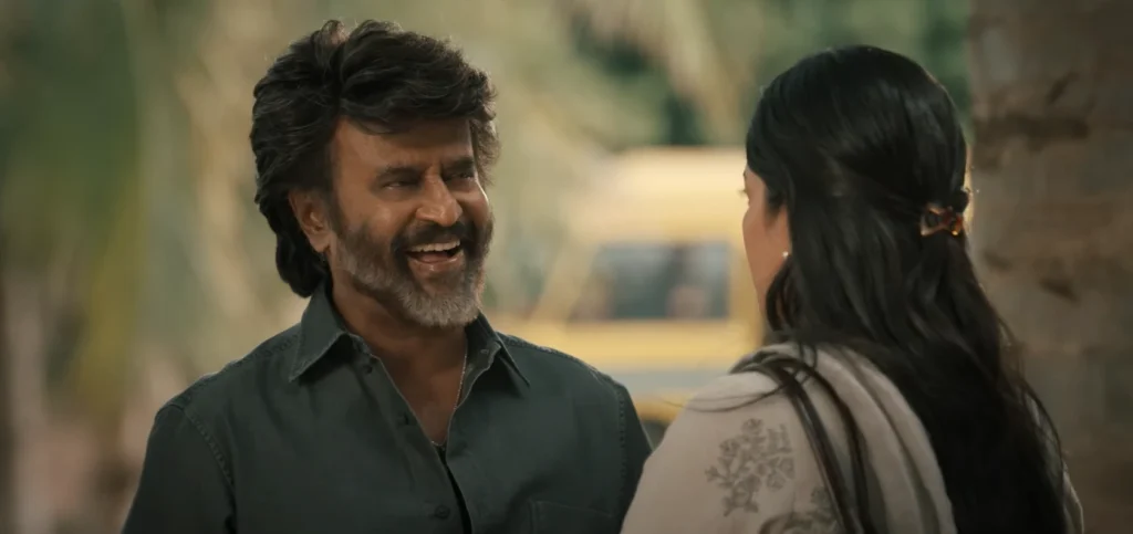 In Coolie Rajnikanth Movie Rajnikanth gives a wide smile while appearing to converse with a woman facing away from the camera.