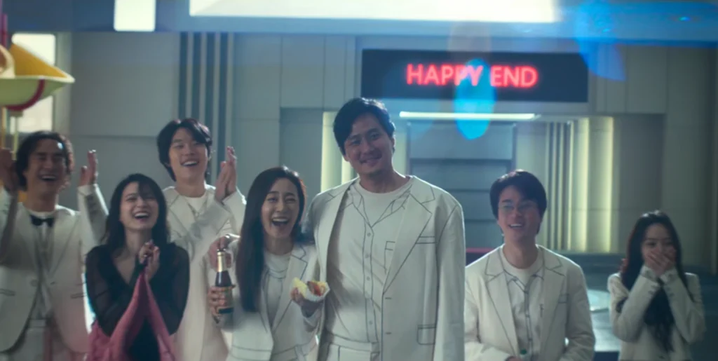 Group of eight smiling Asian actors celebrating the end of "The 8 Show", with "Happy End" neon sign in background.